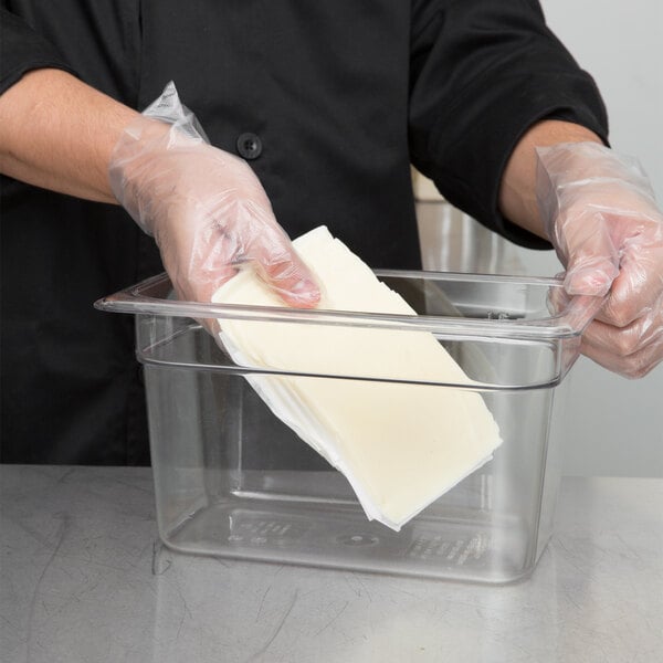A person wearing gloves placing butter in a Cambro clear plastic food container.