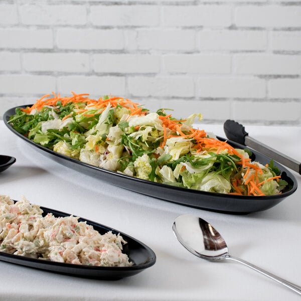 A black Siciliano oval platter with salad on a table.