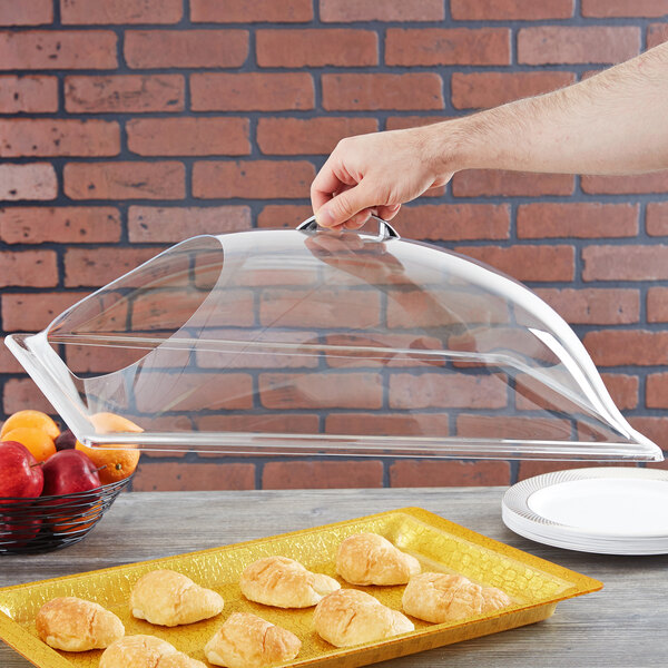 A hand holding a clear Carlisle cover over a tray of pastries.