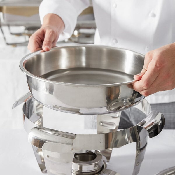 A person holding a stainless steel water pan for a chafer.