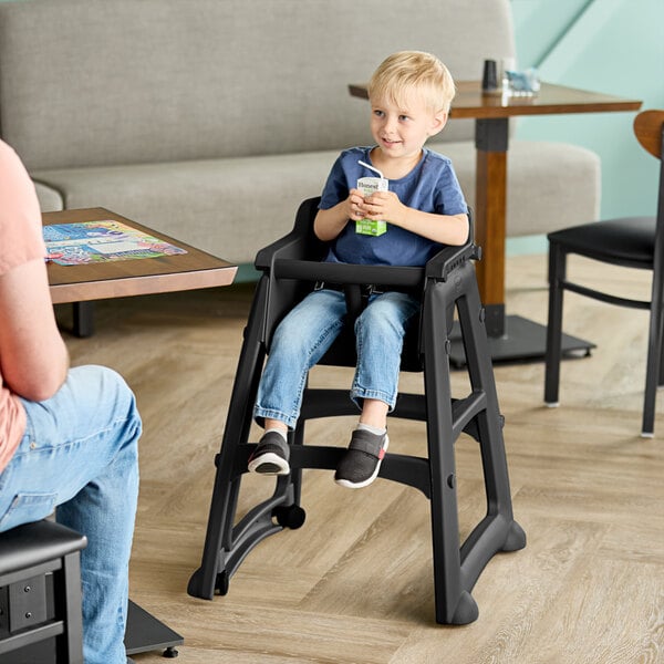 A black restaurant high chair with wheels, shown in use by a child at a dining table.