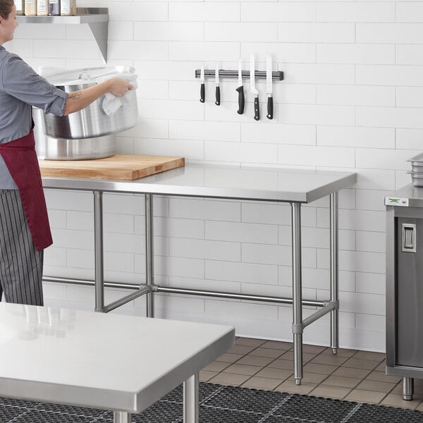 A woman in an apron using a Regency stainless steel work table in a kitchen.