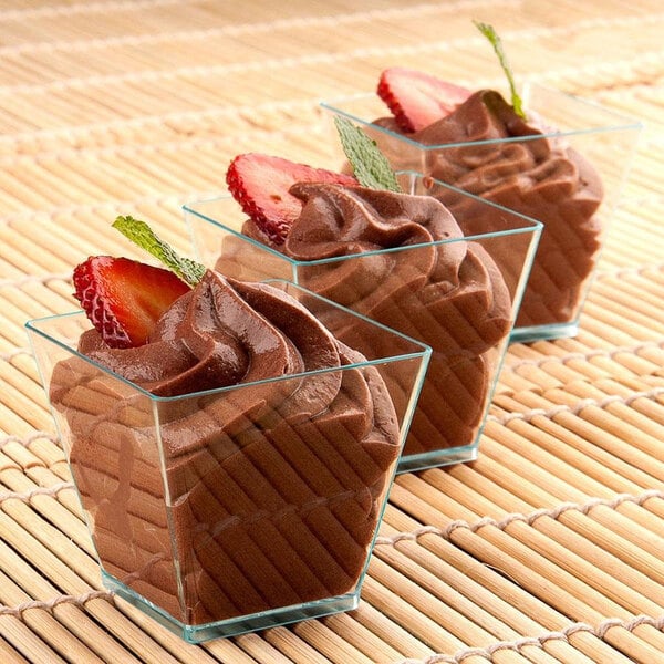 Chocolate mousse in three green plastic square serving dishes, each with a strawberry and mint leaf