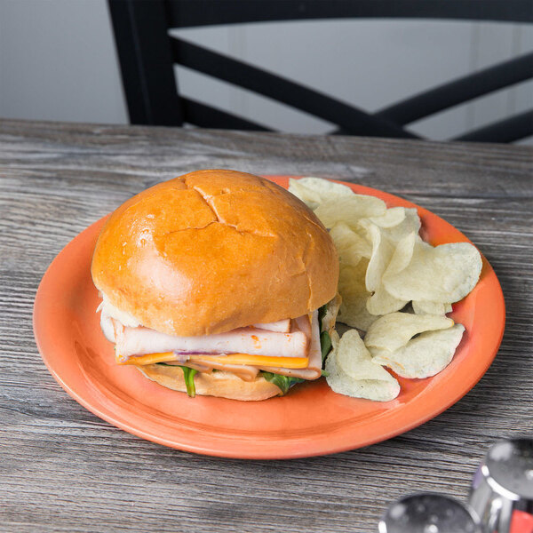 A plate of food with a sandwich and chips on a GET Pumpkin Diamond Harvest plate.