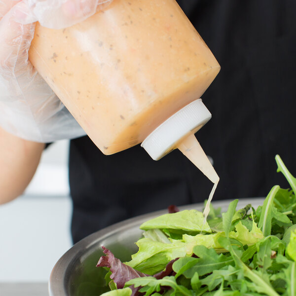A clear plastic squeeze bottle dispensing dressing onto a bowl of salad greens.