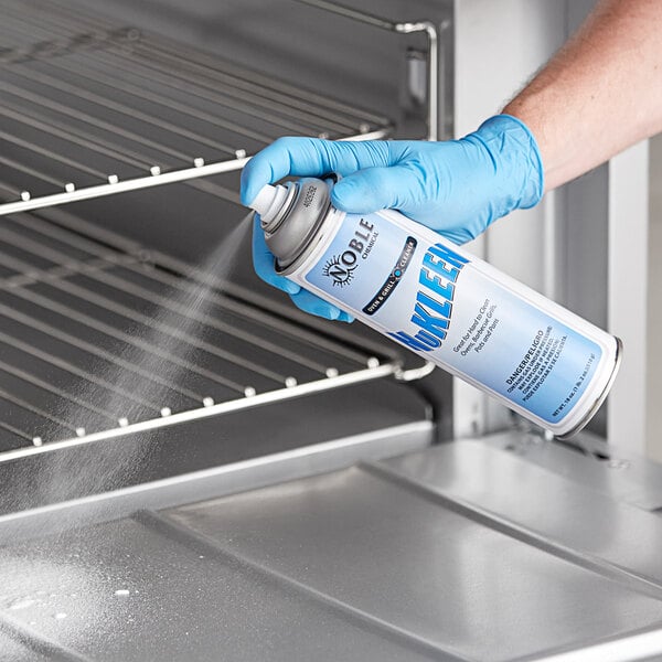 A person in blue gloves using Noble Chemical Nukleen spray on an oven.