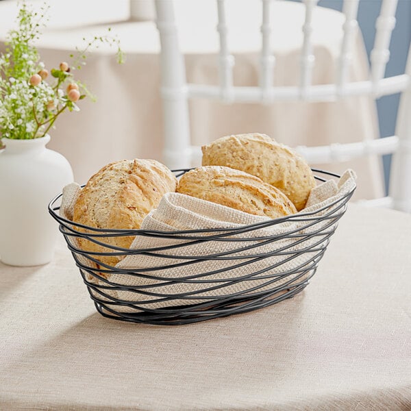 A Tablecraft black wire basket with bread on a table.