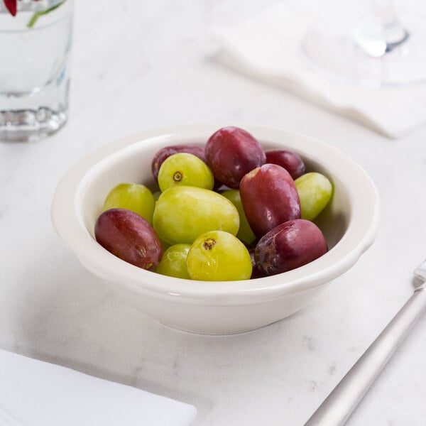 A CAC ivory scalloped edge monkey dish filled with grapes on a table.