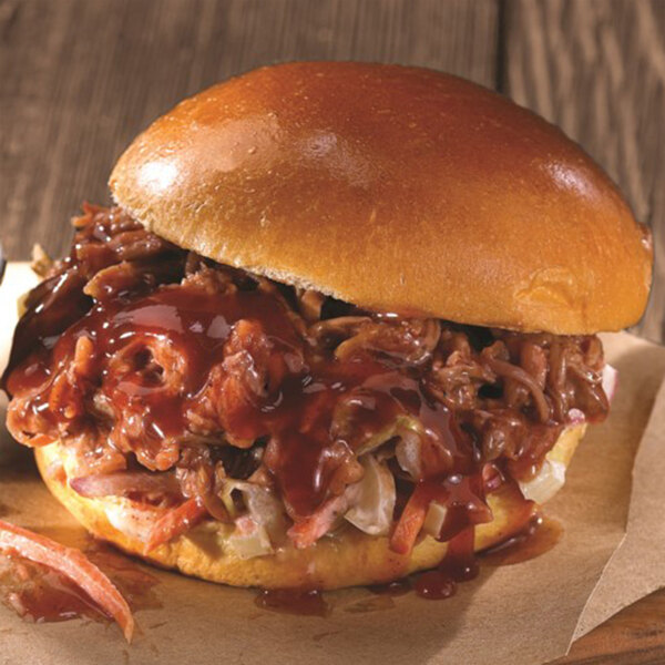 A pulled pork sandwich with malt vinegar on a table in a stadium concession stand.