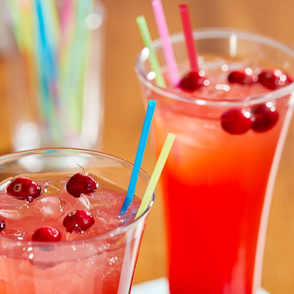 A glass of pink cranberry juice with a neon sip straw and ice with a straw holder.