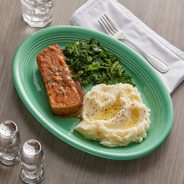 A Tuxton Cilantro oval china coupe platter with a plate of food on a table.