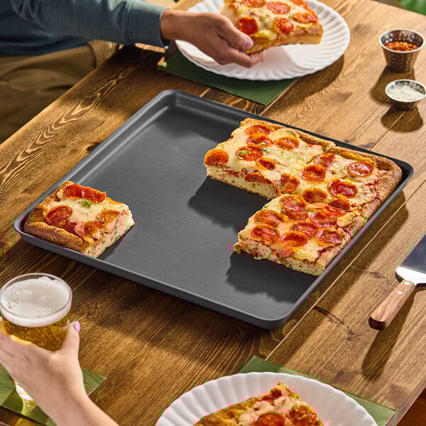 A square hard coat aluminum pizza pan with raised edges, partially filled with pepperoni pizza.