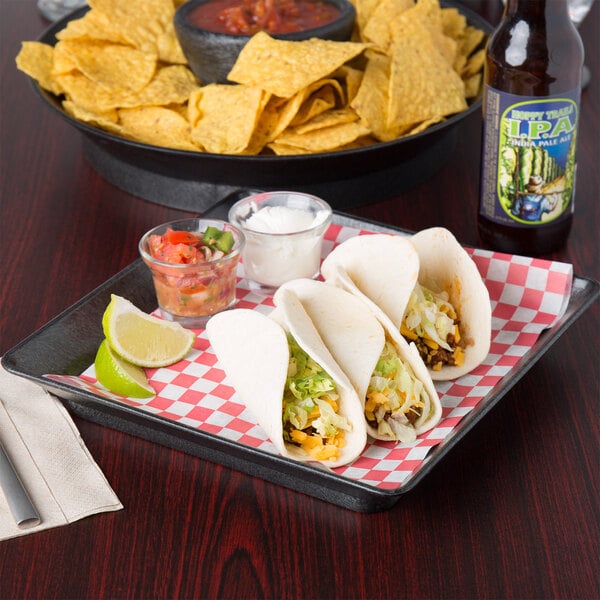 A plate of tacos and chips served on a red and white checkered HS Inc. square deli server.