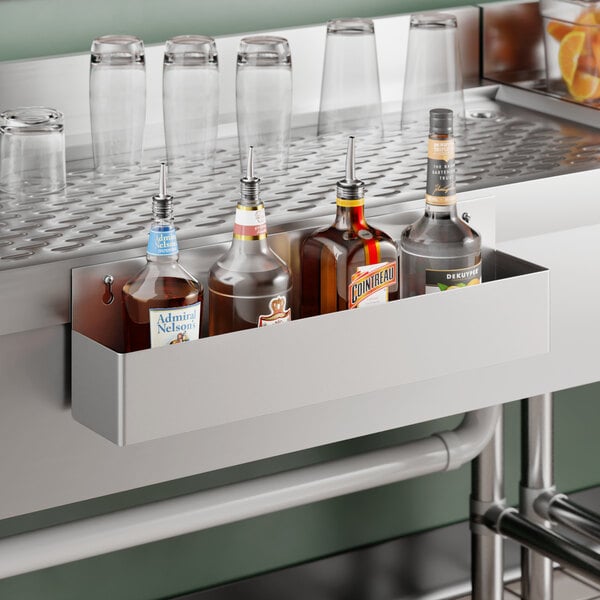 A stainless steel single tier speed rail mounted to a bar counter, holding several liquor bottles.