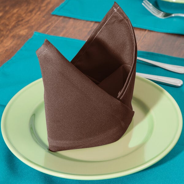 A folded brown Intedge cloth napkin on a plate with a fork and knife.