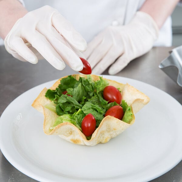 A gloved hand adds a cherry tomato to a salad in a Chicago Metallic tortilla bowl.