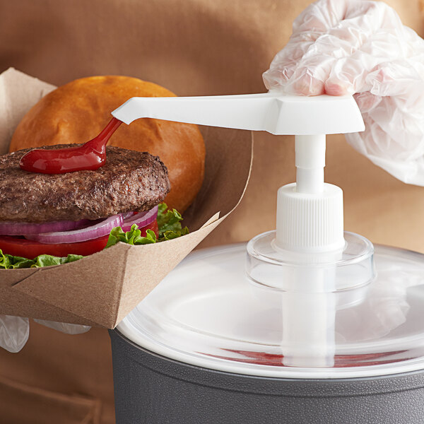 A person using a Carlisle 1/2 oz. pump to put ketchup on a burger.