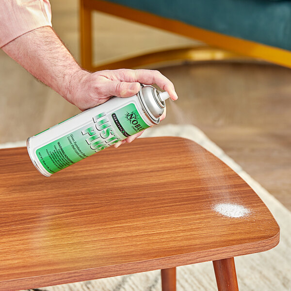 A person using Noble Chemical Luster Plus aerosol wood polish on a wooden table.