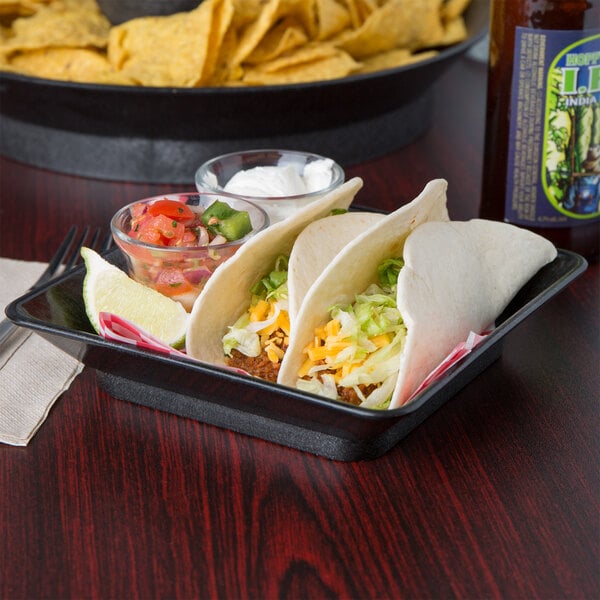 A black tray with tacos, salsa, and limes on it.