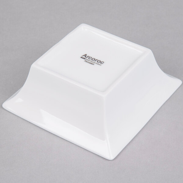 An Arcoroc white square flared bowl with a black logo.
