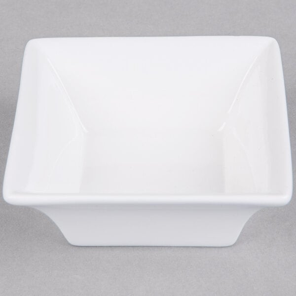 An Arcoroc white square bowl on a gray background.