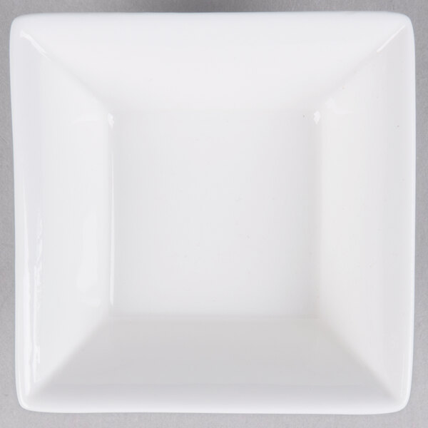 An Arcoroc white square bowl with a flared edge on a gray surface.