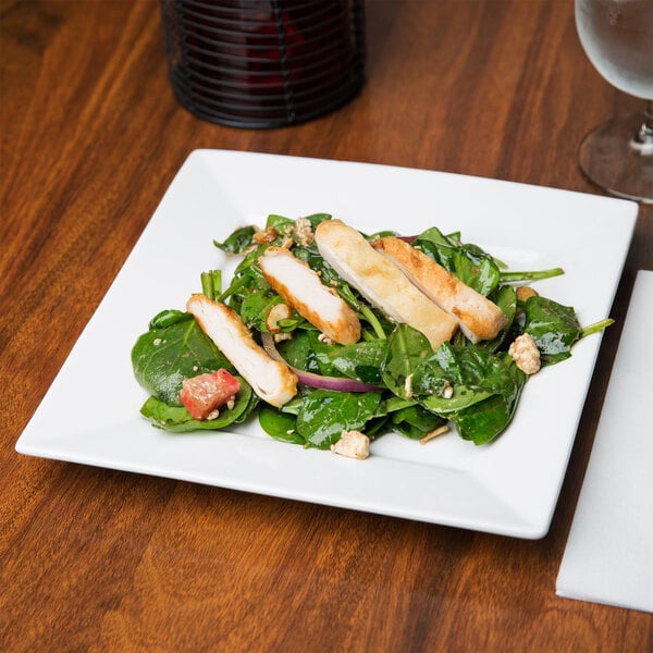 An Arcoroc white porcelain plate with salad, chicken, and vegetables on it.