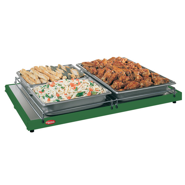 A Hatco Glo-Ray heated shelf with trays of chicken wings, pasta, and bread sticks on a table outdoors.