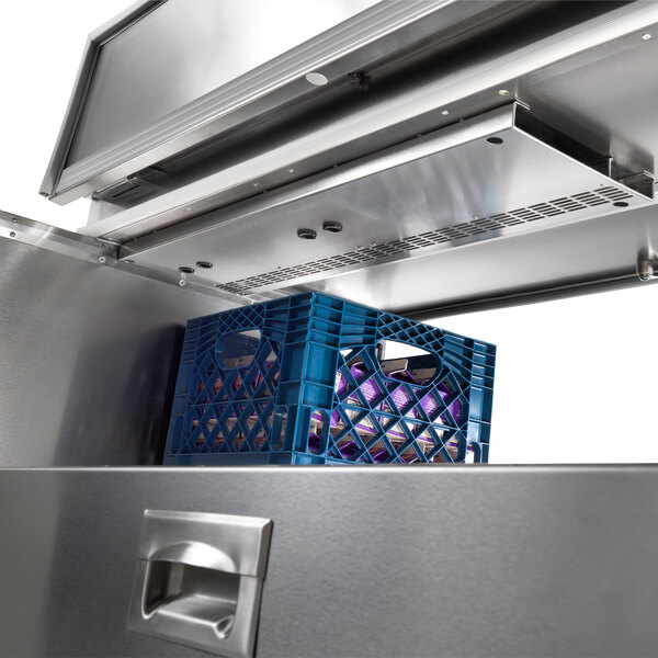 A metal drawer with a blue plastic shelf and a blue grid inside a Traulsen school milk cooler.
