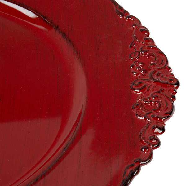 A close up of a red Charge It by Jay plastic charger plate with a carved edge.