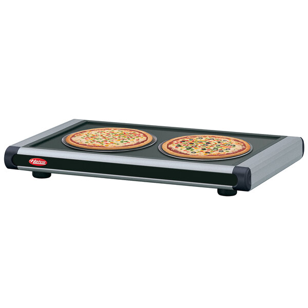 Two pizzas on a black and silver tray on a Hatco heated shelf.