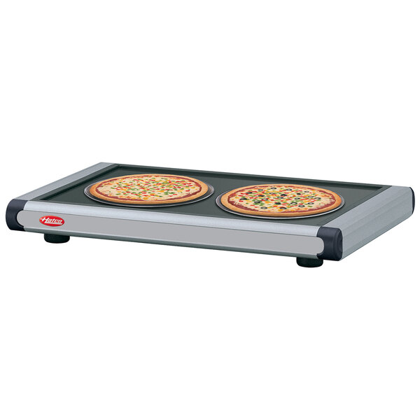 A Hatco heated shelf with two pizzas on a black tray.