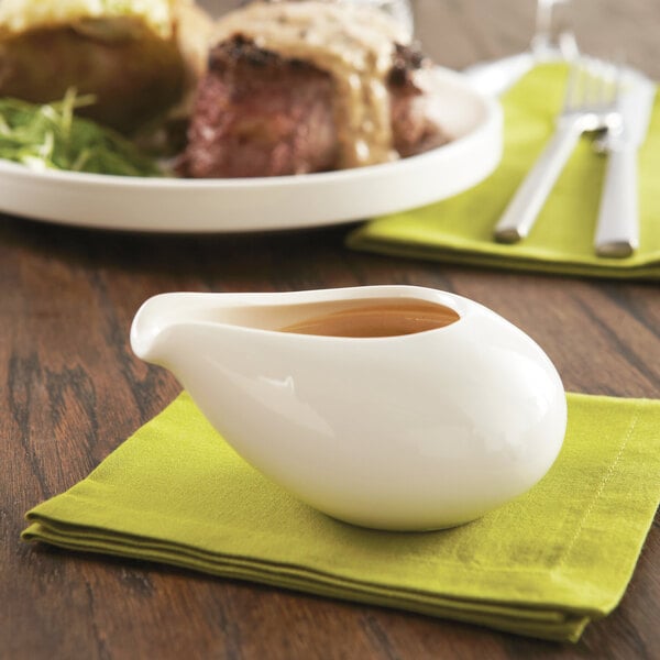 A white porcelain server with brown liquid on a plate of food.