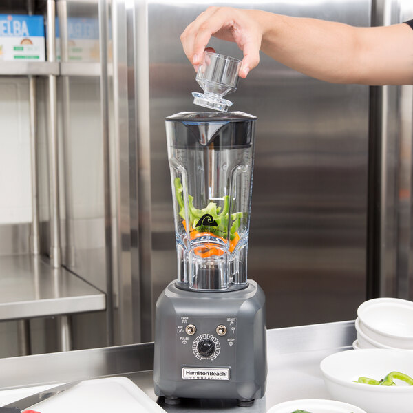 A person preparing a drink in a Hamilton Beach food blender on a counter in a smoothie shop.