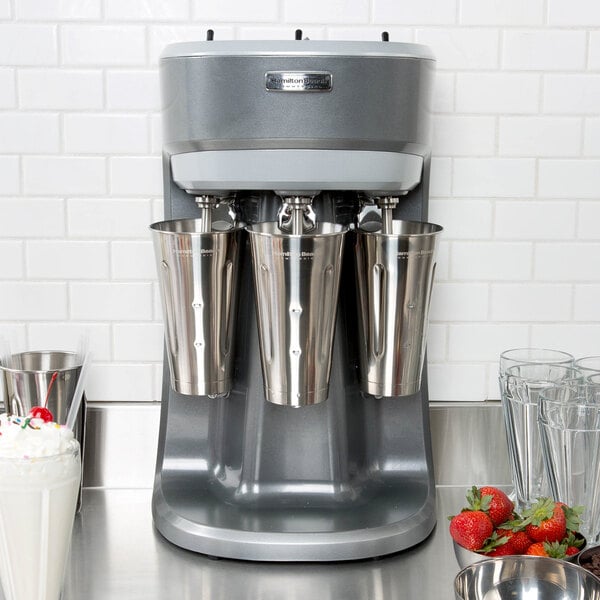 A Hamilton Beach triple spindle drink mixer with silver cups on the counter.