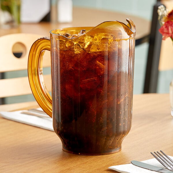 A Carlisle amber polycarbonate beverage pitcher of iced tea on a table.