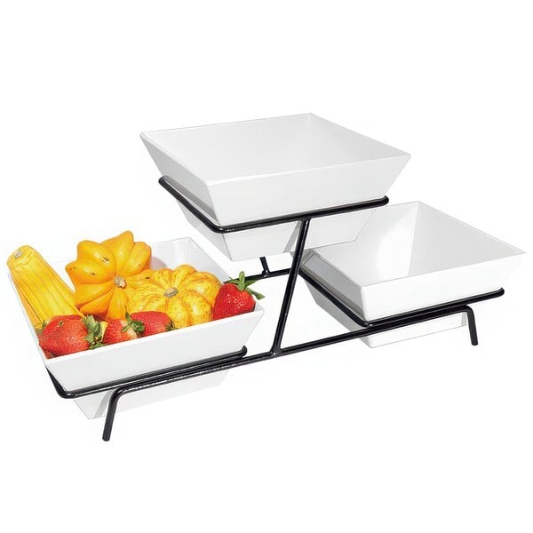 A black two tier metal wire stand with white square bowls of fruit and vegetables.