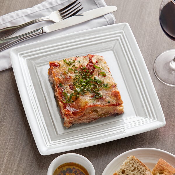 A square white Tuxton Concentrix china plate with a piece of lasagna.