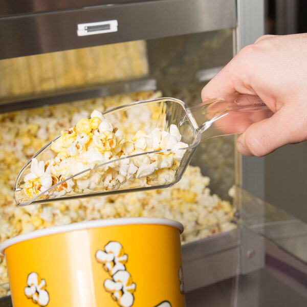 A hand using a Cal-Mil Classic plastic scoop to pour popcorn into a machine.