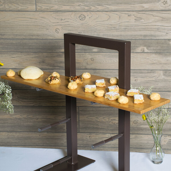 A brown bamboo Cal-Mil shelf on a table in a bakery display with food on it.