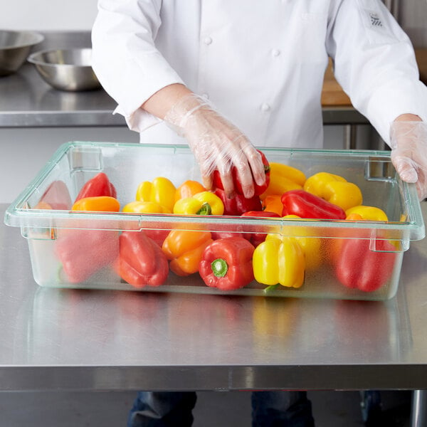 A person in a white coat putting red and yellow bell peppers in a Carlisle green food storage container.