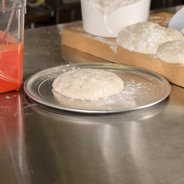 An American Metalcraft heavy weight aluminum pizza pan with dough on it.