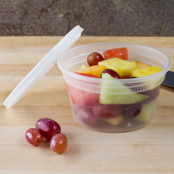 A Pactiv translucent plastic deli container with a lid filled with red grapes on a table.