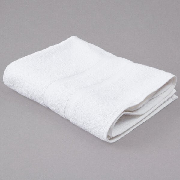A folded white Oxford Gold Dobby bath mat on a gray surface.