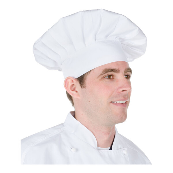 A person wearing a tall, white chef hat and a white chef coat.