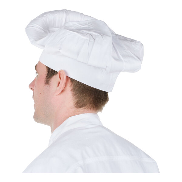 A person wearing a tall, white chef hat and a white coat, viewed from behind.