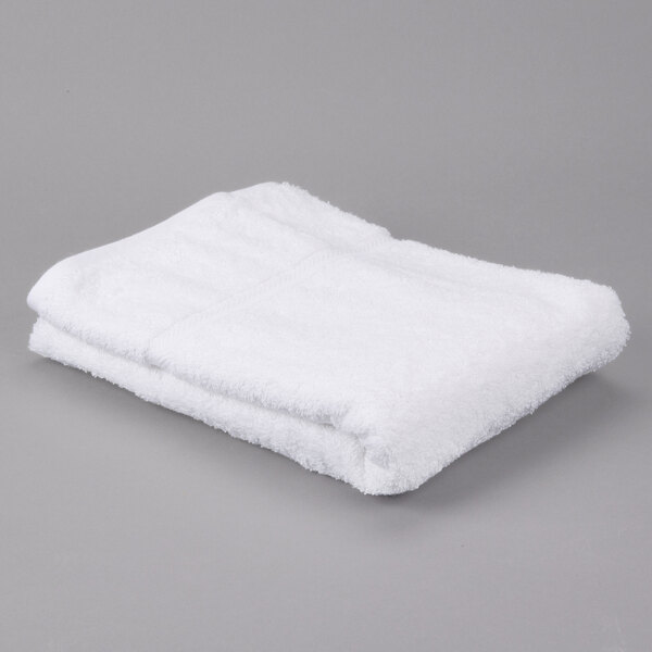 A folded white Oxford Gold bath towel on a gray surface.