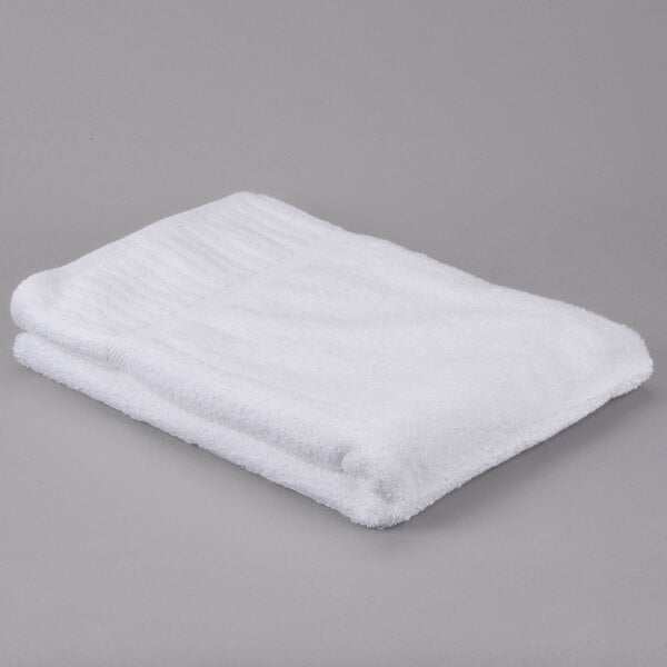 A folded white Oxford Signature bath towel on a gray surface.