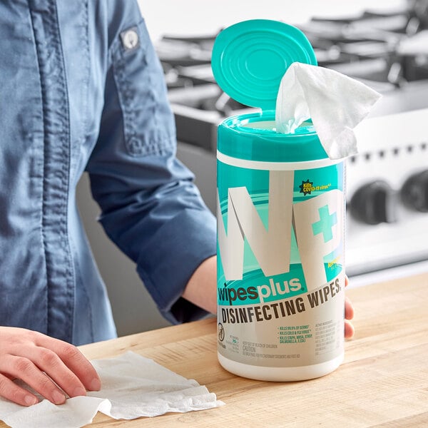 A person holding a white container of WipesPlus lemon scented disinfecting wipes with a blue label.