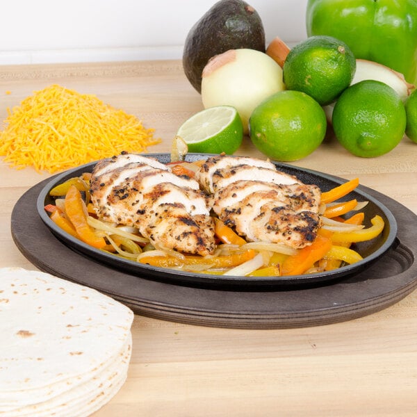 A Lodge oval wood underliner with a plate of chicken fajitas and vegetables on it.